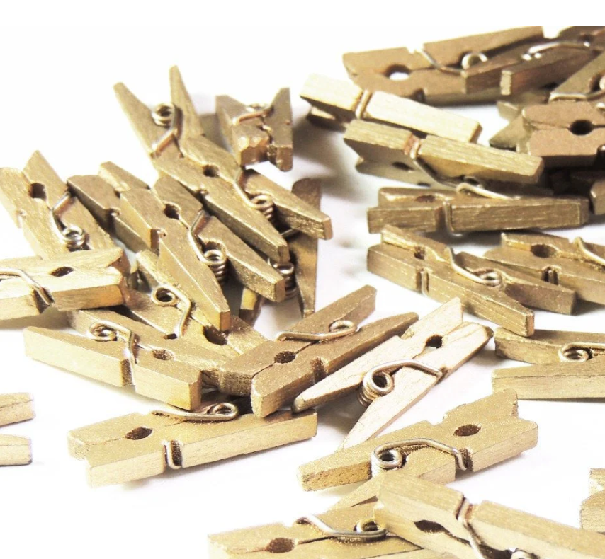 Close-up of mini gold clothespins displayed on a string holding photos and gift tags, showcasing their versatility for crafts, wedding decor, and party decorations